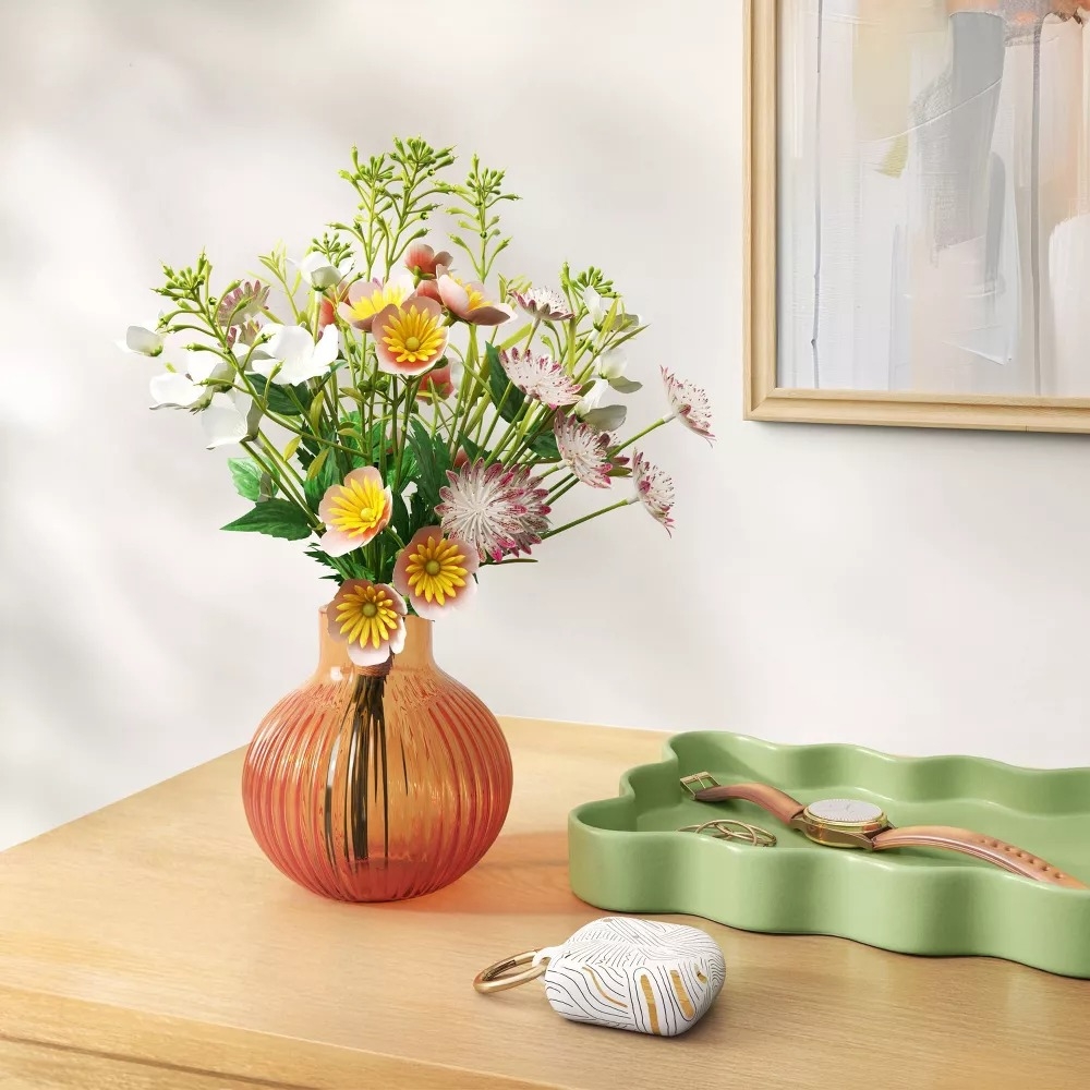 A round orange vase with mixed flowers.