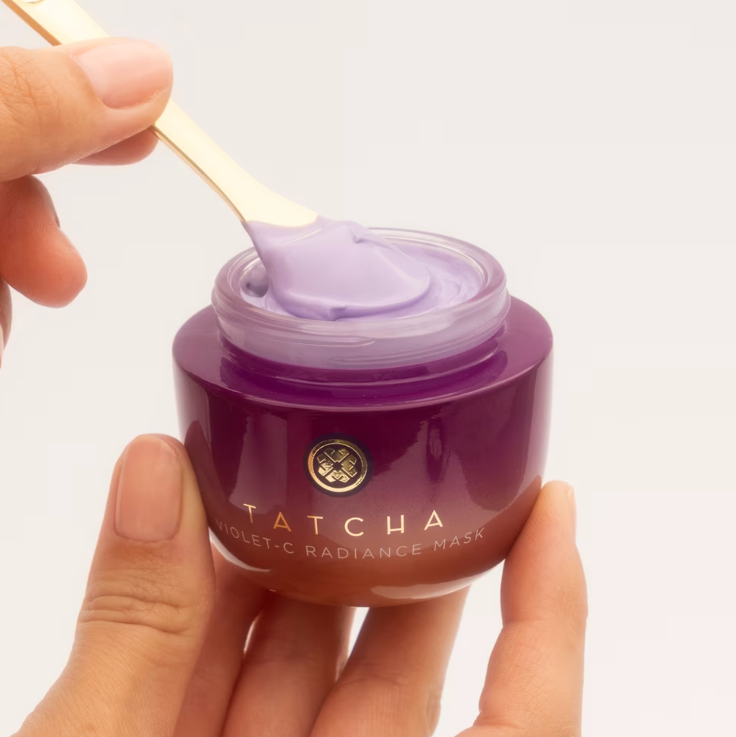 Person scooping violet face mask from a Tatcha jar with a small spatula